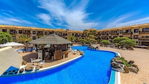 Una piscina con sillones reclinables y una zona de bar, rodeada de edificios de varios pisos con balcones.