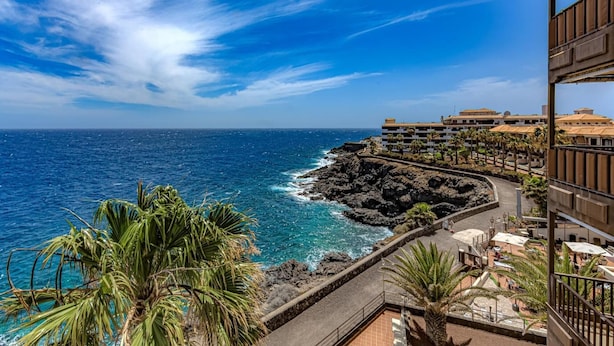 Un hotel frente al mar con vistas al océano, una costa rocosa y un paseo marítimo pavimentado.