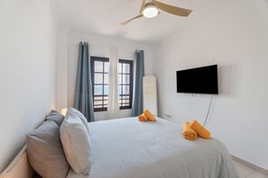 A bedroom with a bed, pillows, a TV, and a ceiling fan. - Vacation 'Atlantic 2 Amazing View' with Sea View, Shared Pool and Wi-Fi (Costa Del Silencio)
