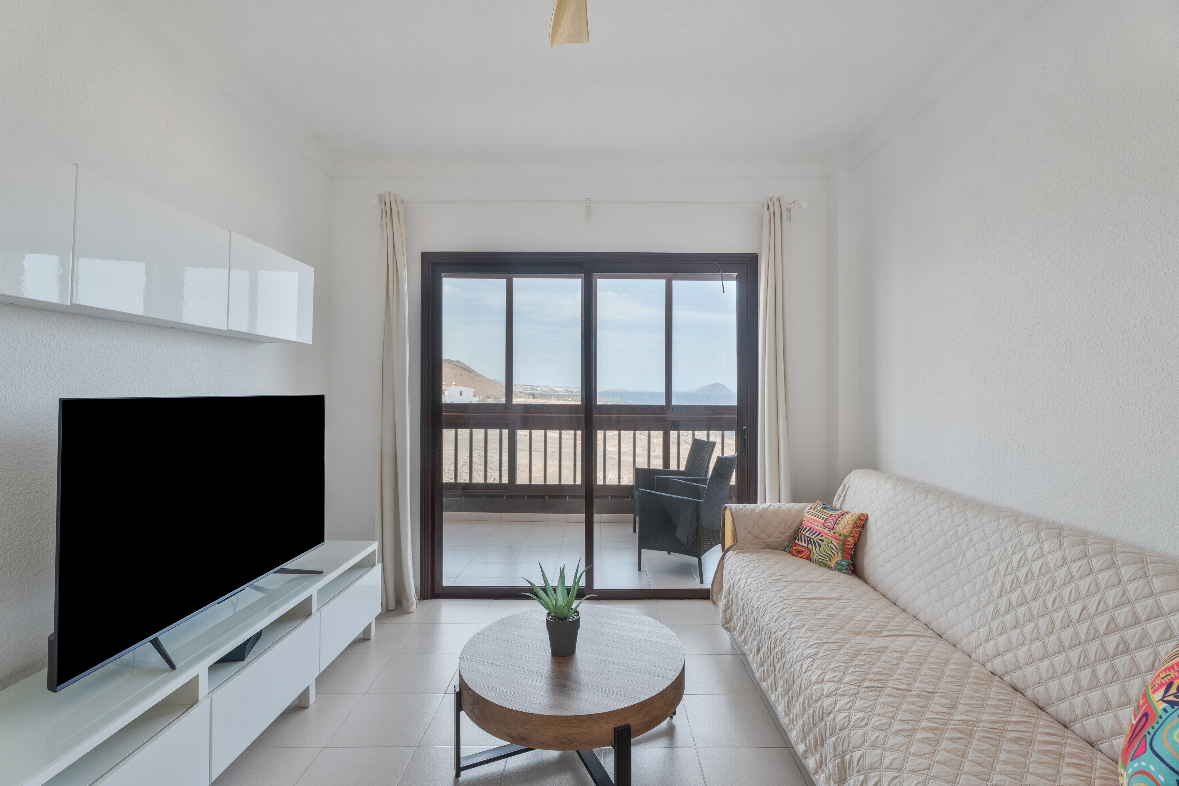 Un salon moderne doté d’un téléviseur à écran plat, d’une table basse ronde en bois, d’un canapé beige et d’un balcon offrant une vue agréable.