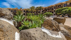 A hotel courtyard with large rocks, palm trees, and a pool. - Vacation 'Atlantic 2 Amazing View' with Sea View, Shared Pool and Wi-Fi (Costa Del Silencio)
