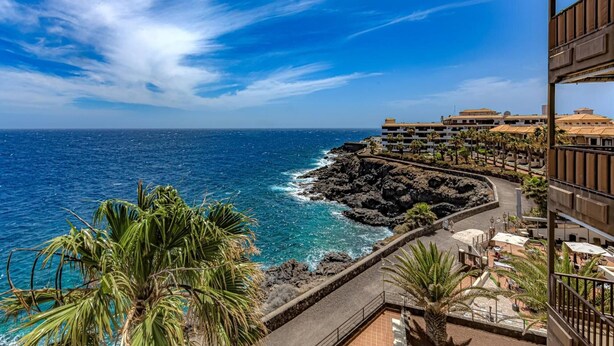 A coastal hotel with a view of the ocean, a rocky shoreline, and a paved walkway. - Vacation 'Atlantic 2 Amazing View' with Sea View, Shared Pool and Wi-Fi (Costa Del Silencio)