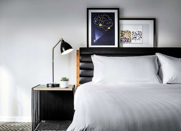 Une chambre à coucher bien rangée, avec un lit, une lampe de chevet, une petite plante et deux œuvres d’art encadrées accrochées au mur.