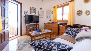 Una sala de estar acogedora con televisión, muebles de madera, un tapete estampado y platos decorativos en la pared.