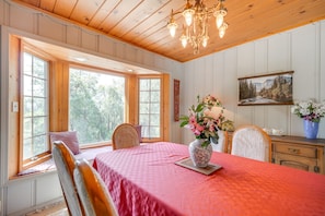 Une pièce avec un plafond en bois, un lustre, une table à manger recouverte d’une nappe rouge et un vase rempli de fleurs.