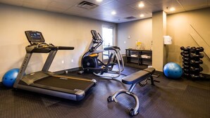 Une salle de sport équipée d’un tapis de course, d’un vélo elliptique, d’un banc de musculation et d’haltères.