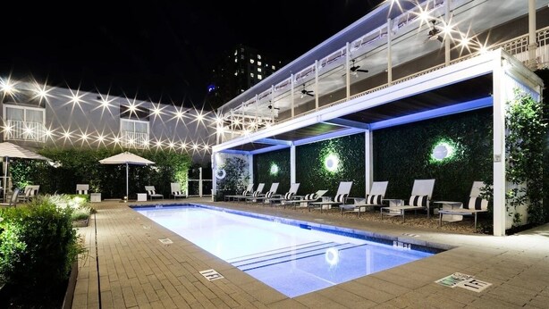 Un espace piscine nocturne avec des chaises longues et des parasols, entouré de verdure et illuminé par des lumières en forme d’étoile.