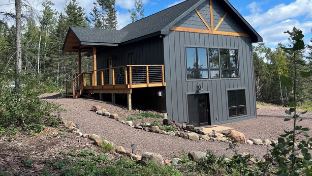 Una cabaña moderna con terraza de madera, ventanas amplias y cimientos de piedra.