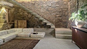 A living room with a stone wall, a white staircase, a white sectional sofa, a wooden cabinet, and a large potted plant. - As Roeles Caión Farm. House ideal for families, beach at 2.5 km. 4 bedrooms (A Laracha)