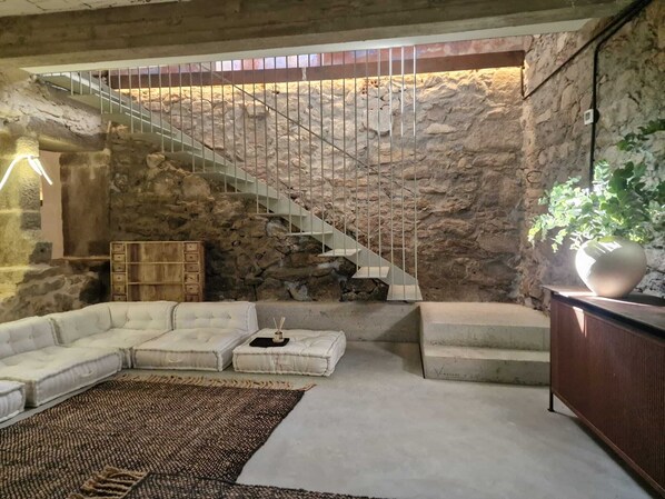 A living room with a stone wall, a white staircase, a white sectional sofa, a wooden cabinet, and a large potted plant.