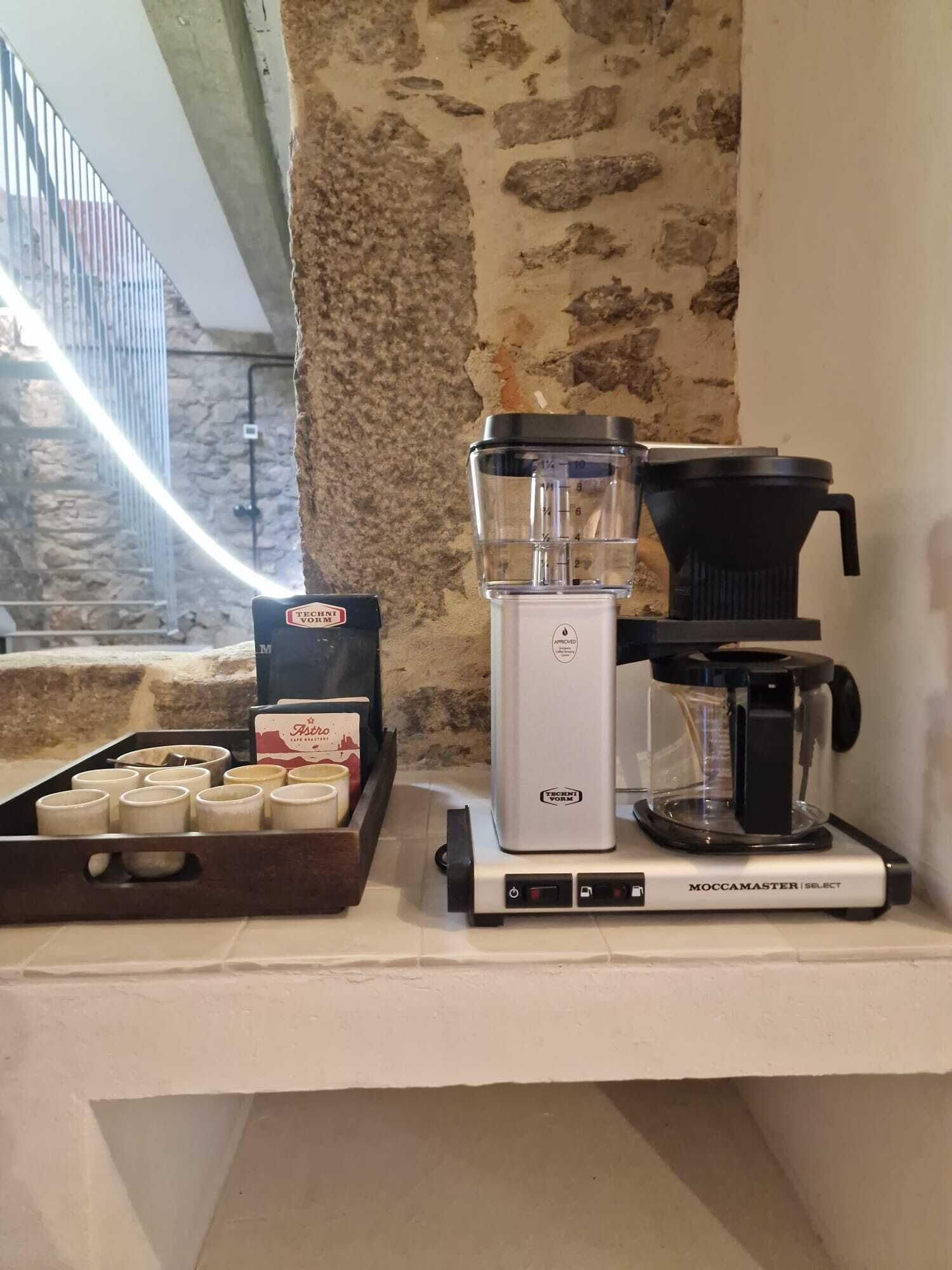 Une machine à café, une cafetière et une assiette de tasses à café sur un comptoir.