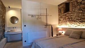 A bedroom with a stone wall, a bed, a bedside table with a lamp, and a bathroom with a sink and mirror. - As Roeles Caión Farm. House ideal for families, beach at 2.5 km. 4 bedrooms (A Laracha)