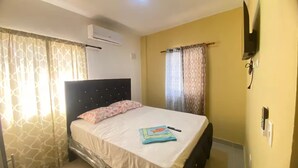 A bedroom with a bed, curtains, an air conditioning unit, a television, and a door lock.