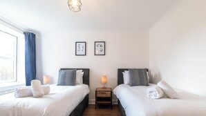 Hotellihuone, jossa on kaksi sänkyä, yöpöytä lampun kanssa ja seinällä tauluja.