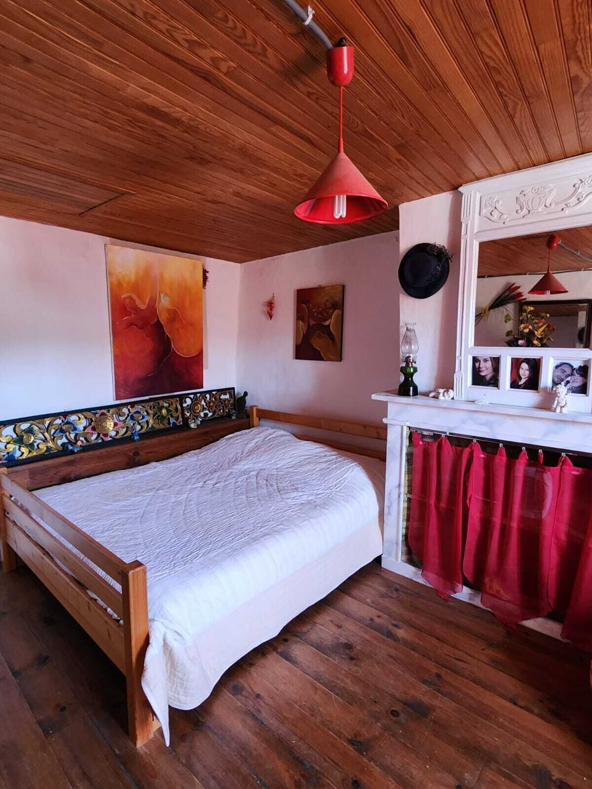 Ein Schlafzimmer mit einem hölzernen Bett, einer roten Pendelleuchte, einer weißen Kommode und einem Spiegel mit Fotos.