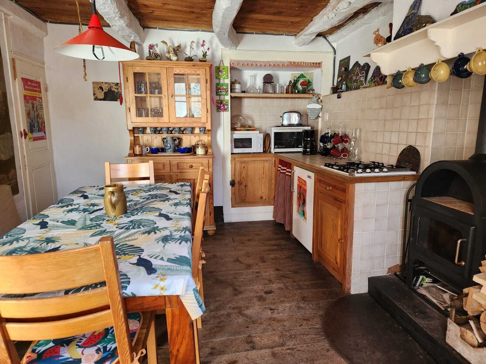 Eine kompakte Küche mit Holzausstattung, einem Esstisch mit Stühlen, einer Mikrowelle, einem Herd und einem Kaminofen.