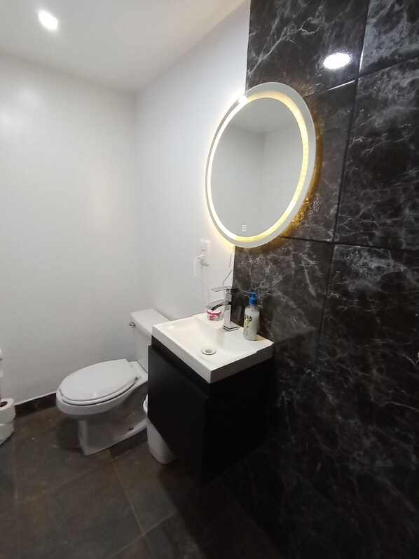 A modern bathroom with a white toilet, a black vanity, and a marble backsplash. - Iguana Co-living (Oaxaca)