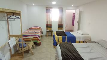 A dormitory room with bunk beds, a wooden wardrobe, a fan, and a window with curtains.