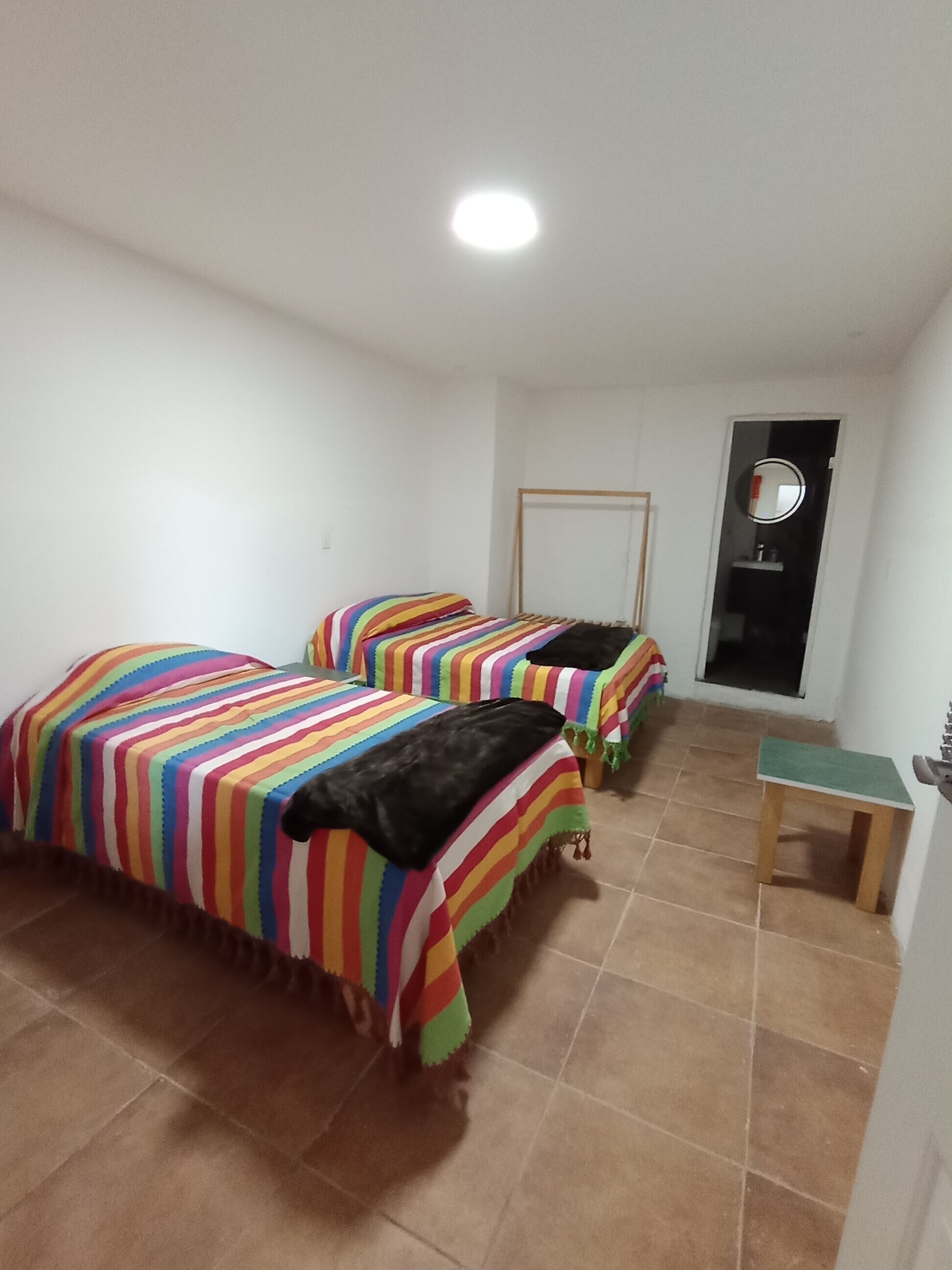 A room with two beds with striped bedding, a small table, and a mirror on the wall.