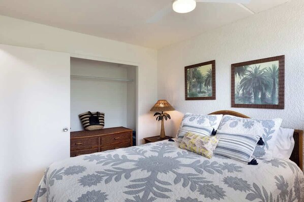 A bedroom with a bed, a nightstand, a lamp, a dresser, and two framed pictures on the wall. - Amazing Fantastic Happy Honu NEW (PKC 106) ~ 3 BR ~ Ground Floor ~ Pool (Kamuela)