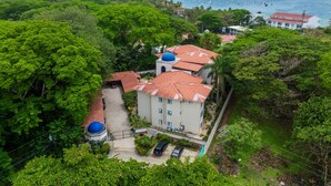 A building with red-tiled roofs and blue domes, surrounded by lush greenery and a coastal view.