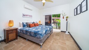 A bedroom with a bed, bedside lamp, ceiling fan, and a view of the outdoors.