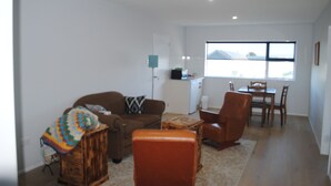 A living room with a sofa, armchair, and coffee table. There is a dining area with a table and chairs. A window provides natural light.