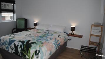 A bedroom with a bed, two bedside tables with lamps, a chair, a wooden shelf, and a ladder.