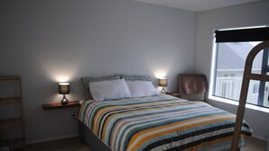 A bedroom with a bed, two bedside lamps, a window, and a wooden ladder.