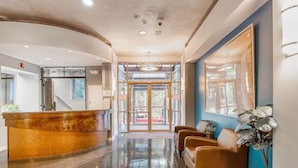 Un'area di accoglienza con una reception in legno a forma curva, una zona salotto con poltrone in pelle e un ingresso in vetro verso un'area esterna.