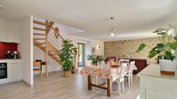 A modern kitchen with a wooden staircase, a dining area with a floral tablecloth, and a stone wall.