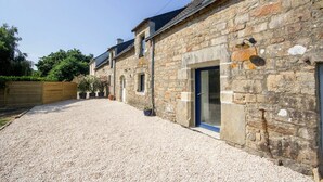 A stone building with a gravel driveway, a wooden fence, and potted plants.