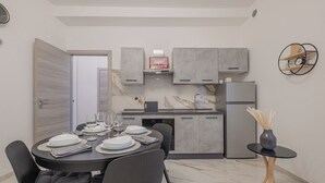 A modern kitchen with grey cabinets, a built-in oven, and a refrigerator. There is a dining table set with plates and glasses. - Rome Apartment Tuscolana Area (Metro A) ~Petit House~ (Roma)