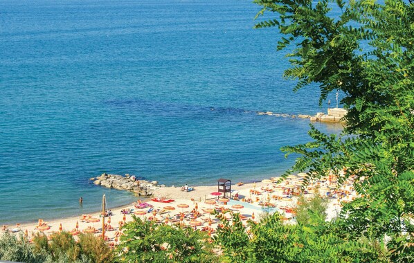 A beach with umbrellas and sun loungers, a rocky shoreline, and a clear blue sea.