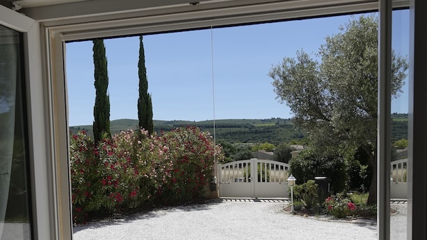 Vista a través de una ventana que muestra un jardín con un camino de grava, una reja y una colina al fondo.