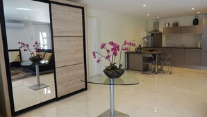 Una cocina moderna con zona de comedor, una mesa de vidrio con una orquídea en maceta y un muro espejado que refleja la habitación.