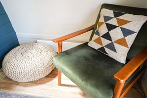 A green upholstered chair with a geometric-patterned pillow, a round woven ottoman, and a wooden armrest. - Luxury Cabin in Rural Hampshire without Pergola (Chawton)