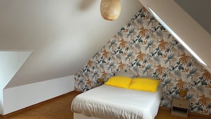 A bedroom with a sloped ceiling, a bed with white bedding and yellow pillows, a small bedside table, and a patterned wall.