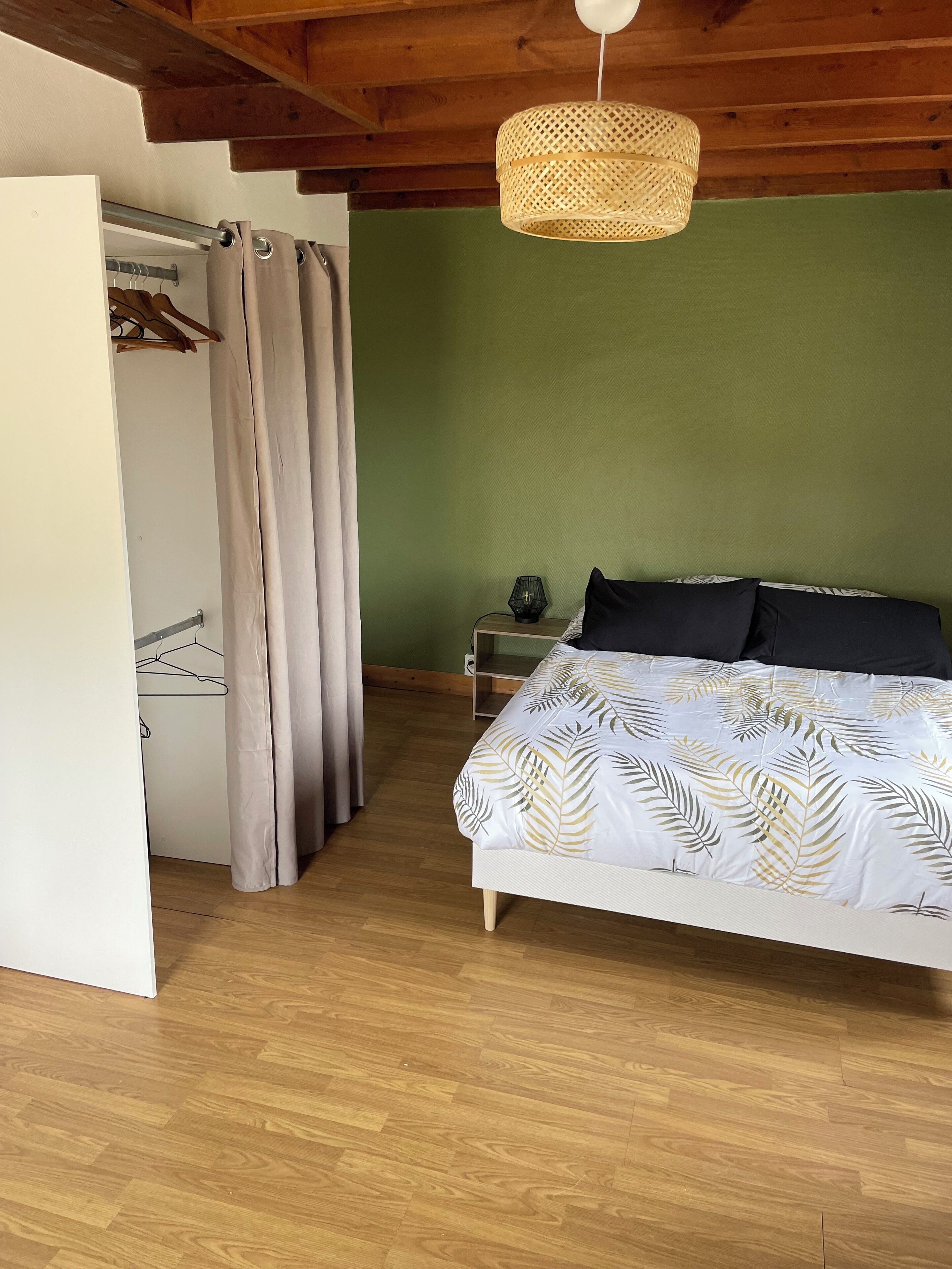 Une chambre à coucher avec un lit, une table de chevet, une lampe suspendue, une armoire et un rideau.