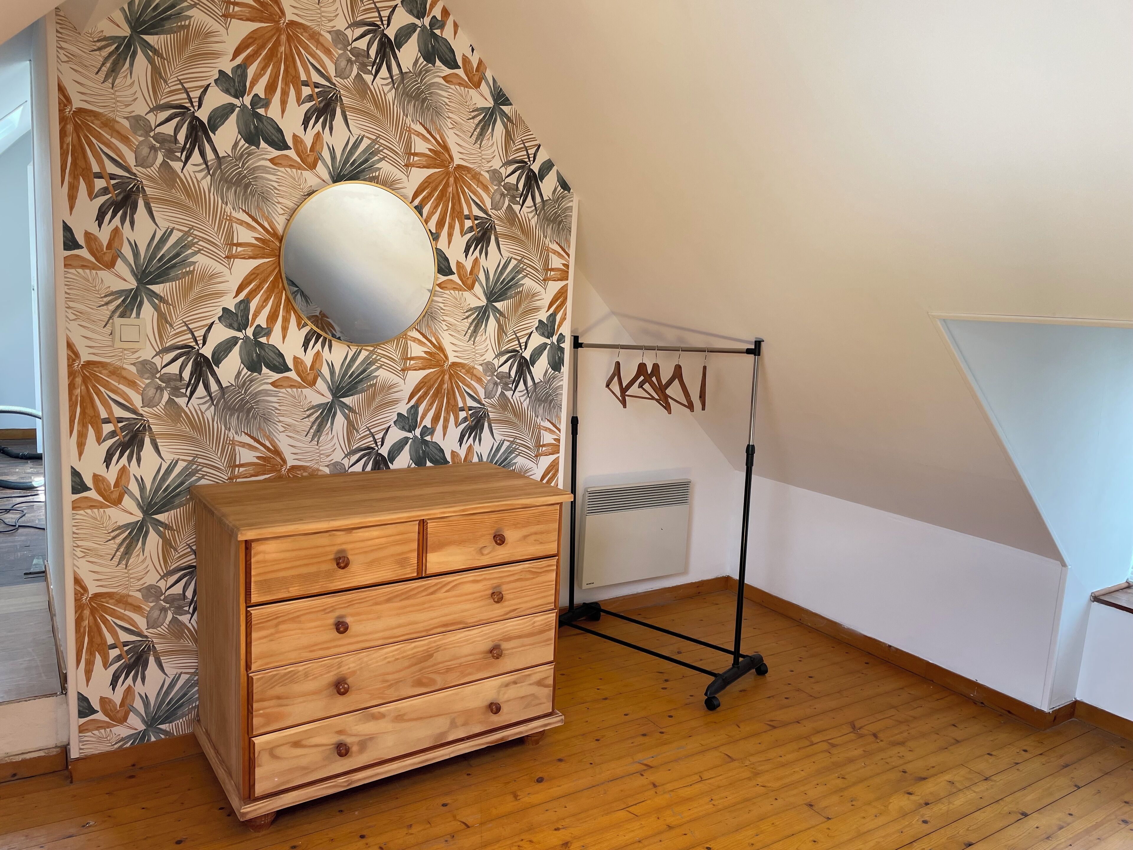 Quarto com penteadeira de madeira, espelho e parede com padrão de folha tropical.