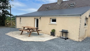 A small building with a gravel driveway, a picnic table, a potted plant, and a small table with a chain-link fence.