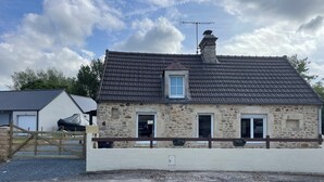A stone house with a dark tiled roof, a chimney, and a gated entrance.