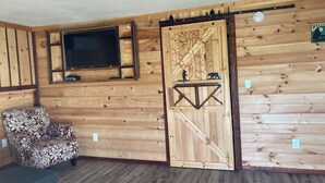 A wooden interior with a TV mounted on the wall, a patterned armchair, and a sliding door with a bear design.