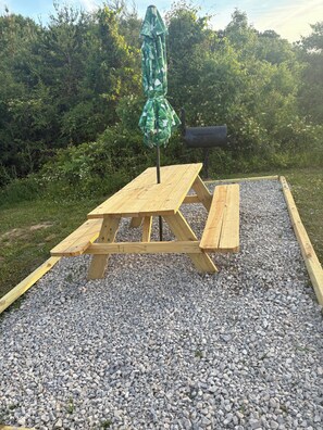 A wooden picnic table with an umbrella, surrounded by gravel and greenery. - Fabulous cabin with AC in Sevierville (Sevierville)