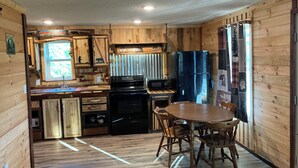 A compact kitchen with wooden walls, a black refrigerator, a microwave, and a dining table with chairs.
