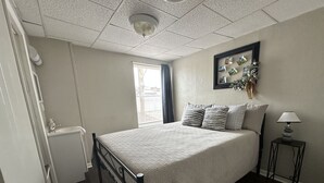 A bedroom with a bed, a nightstand, a lamp, a window with blinds, and a wall-mounted picture frame. - Newly renovated 2 bdrm apartment in downtown (24) (Coshocton)