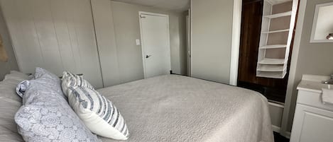 A bedroom with a bed, pillows, a wardrobe, a mirror, and a shelf.