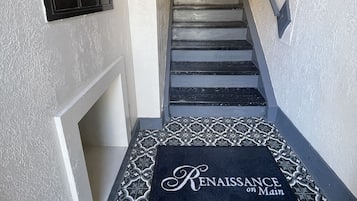 A staircase with a patterned doormat at the bottom and a set of numbered lockers on the wall.