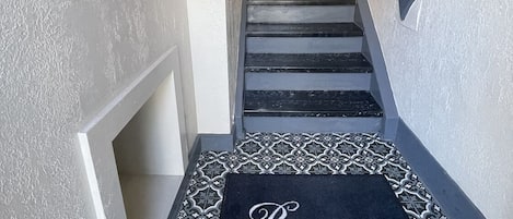 Un escalier, avec un paillasson à motifs au bas, et une rangée de casiers numérotés fixée au mur.