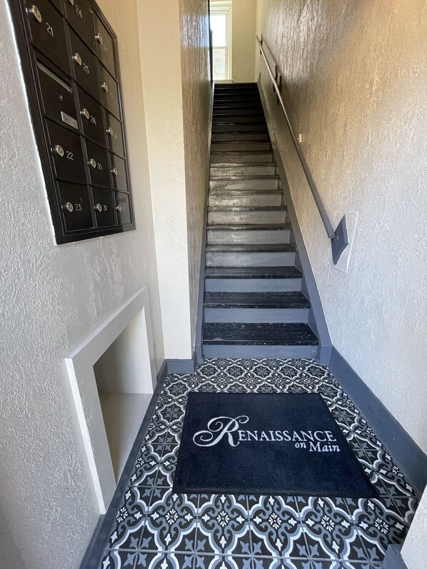 Una escalera con un felpudo estampado al pie y varios taquillones numerados en la pared.